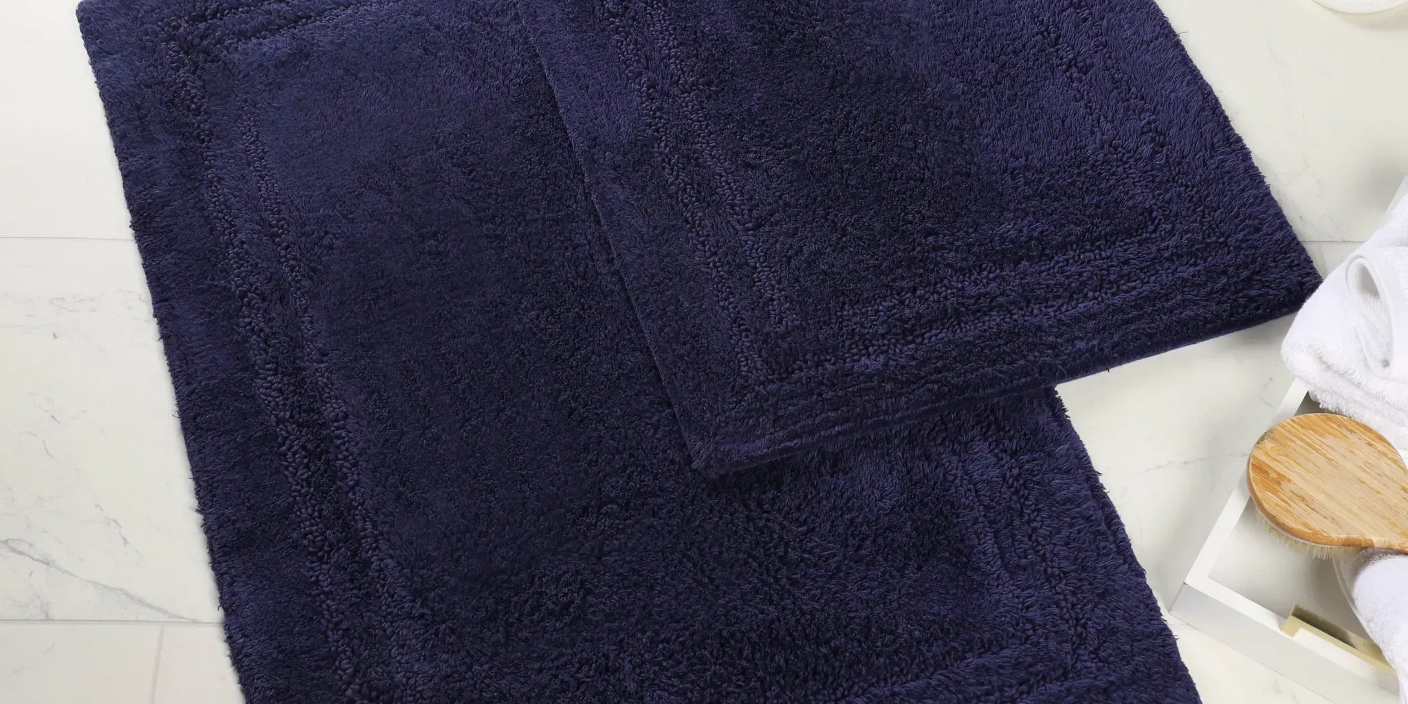 Superior navy cotton bath rug set on a marble bathroom floor with slippers and a bath brush